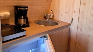 Cocina compacta con techo de madera, cafetera, lavabo y refrigerador empotrado.