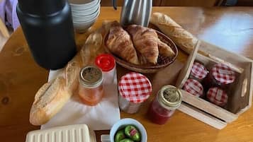 Ein Holztisch mit Croissants, Marmeladengläsern, einer Kaffeekanne und einer Gebäckauslage.