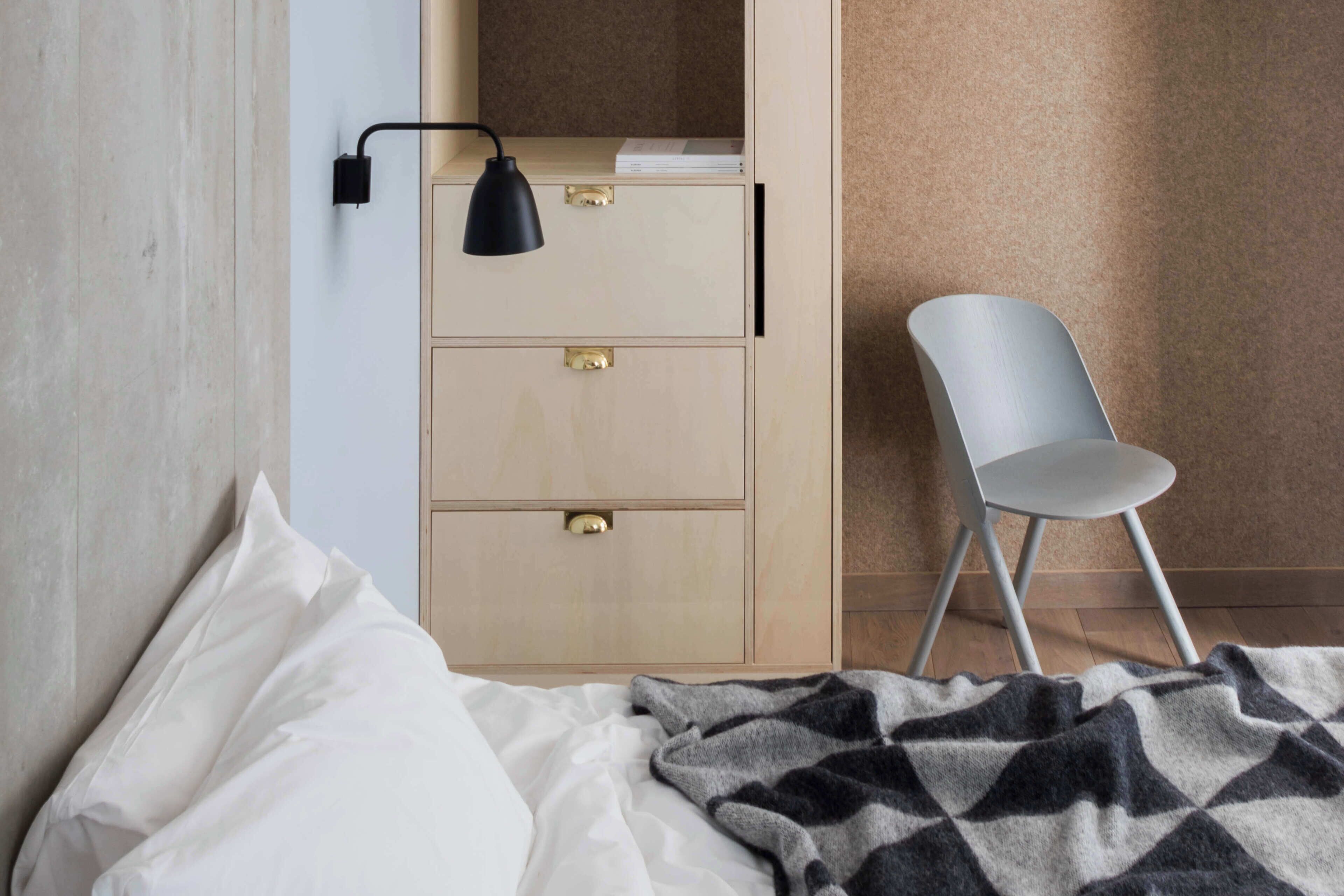 Un dormitorio con una cama, un aparador de madera con cajones, una silla y una lámpara de pared.