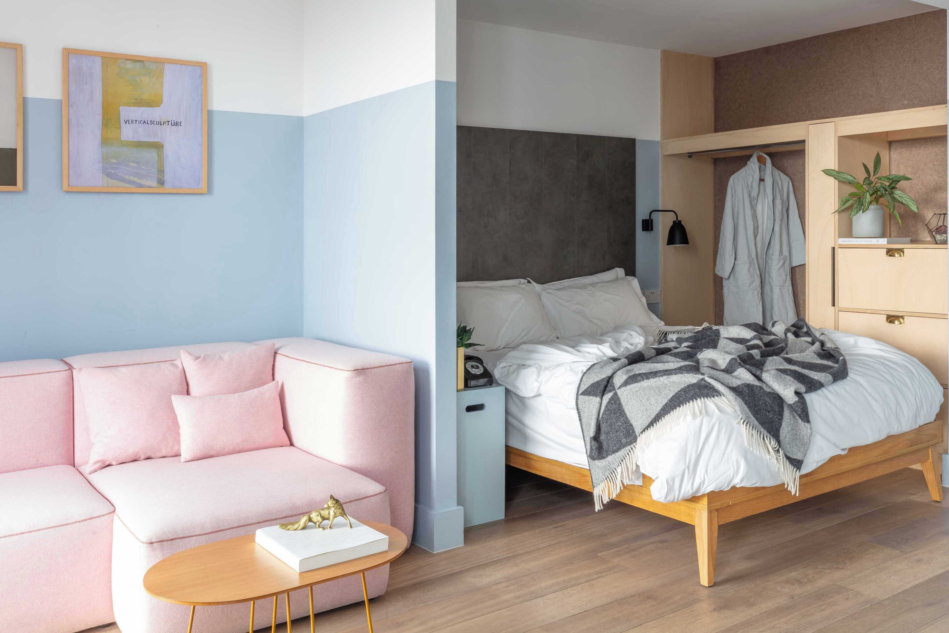 Quarto moderno com sofá rosa, cama de madeira, mesa de cabeceira e prateleira na parede com uma planta.