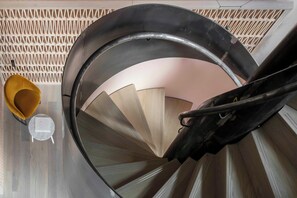 A spiral staircase with a modern design, a yellow chair, and a small table at the top. - Leman Locke (London)