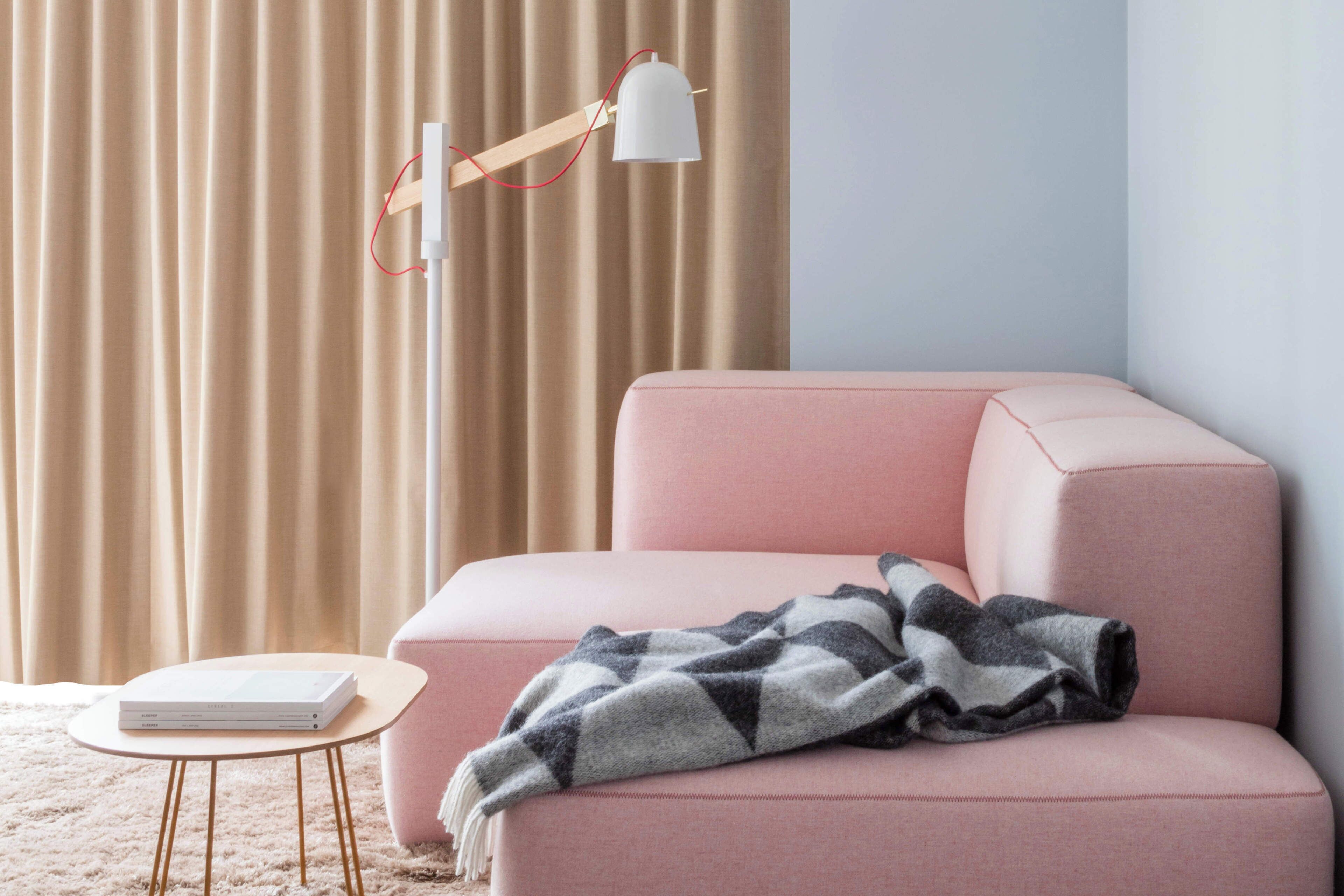A room with a pink sofa, a small round table, a lamp, and a curtain.