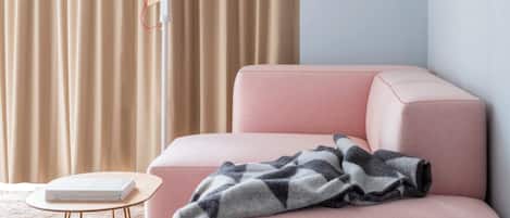 A room with a pink sofa, a small round table, a lamp, and a curtain.