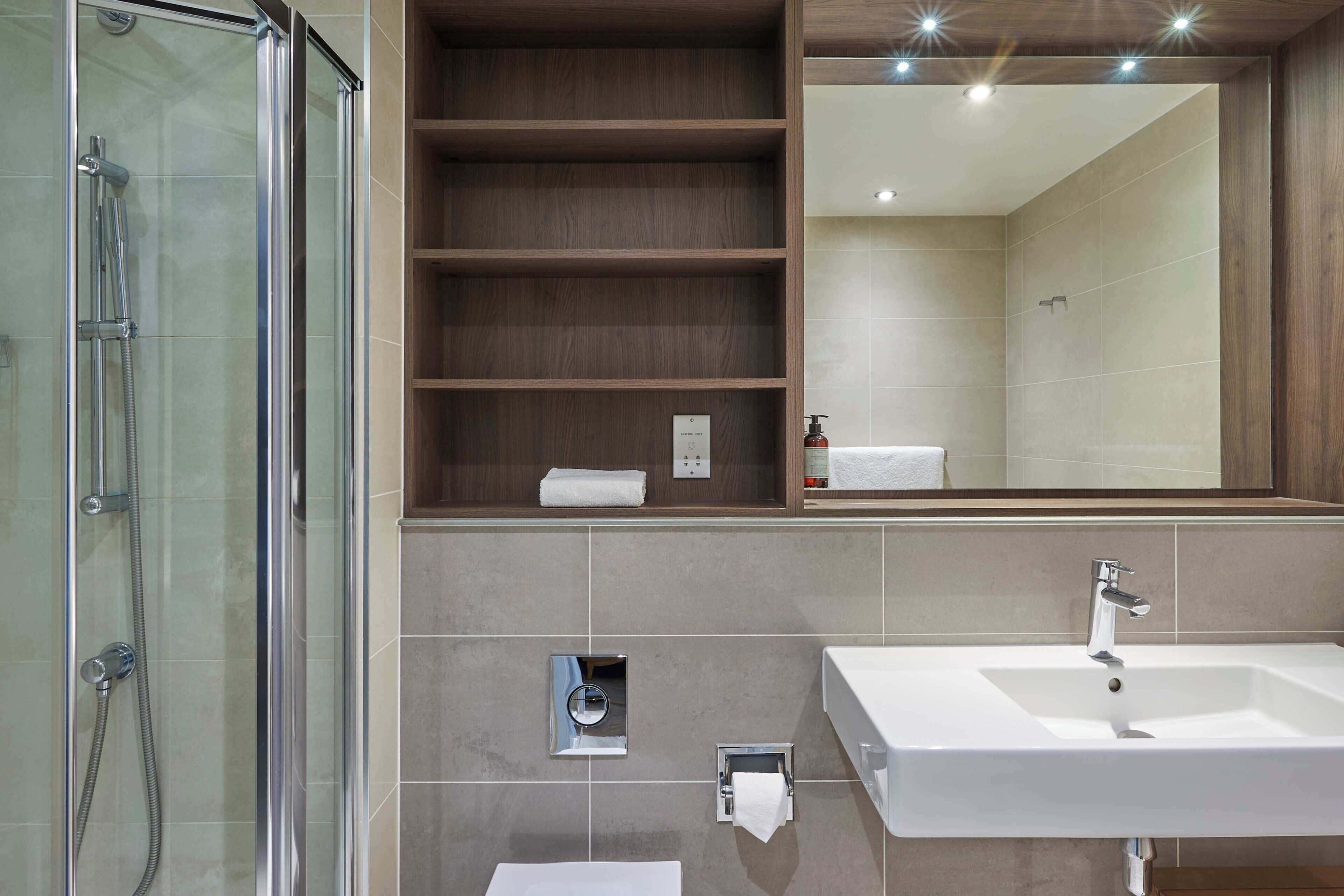 A modern bathroom with a glass-enclosed shower, a large mirror, and a built-in sink.