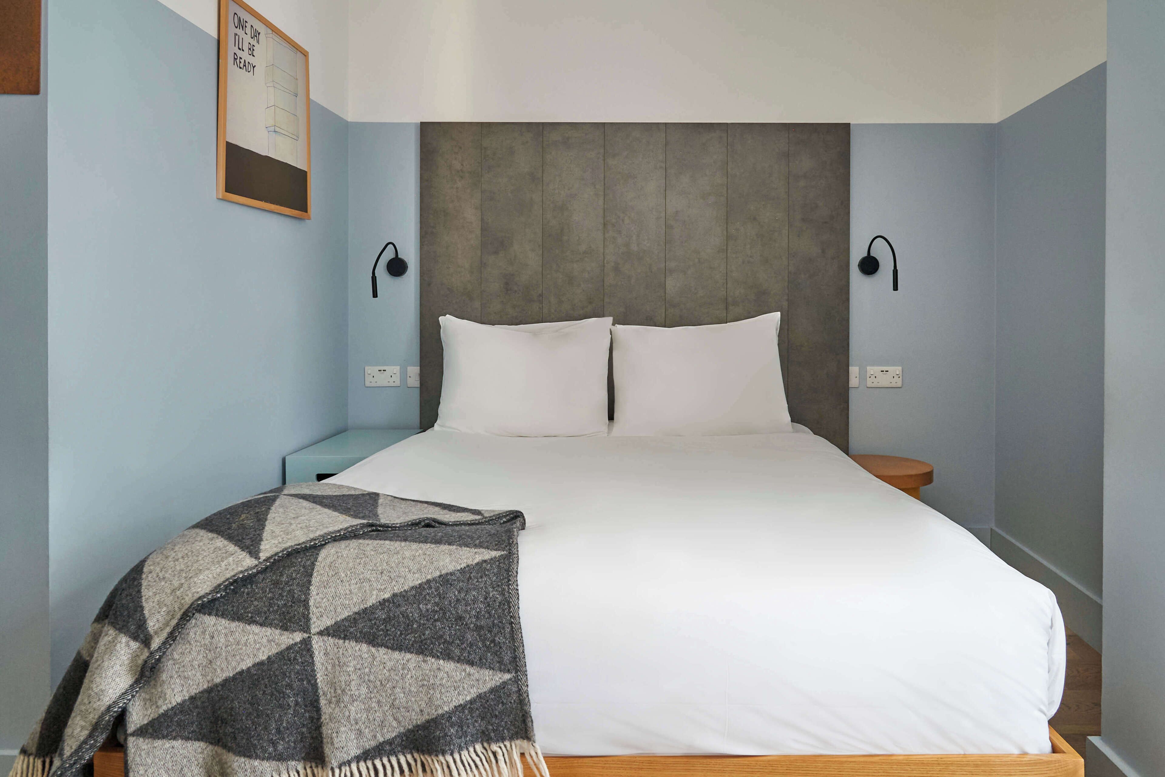 A bedroom with a bed, two bedside tables, a wall-mounted lamp, and a blanket.