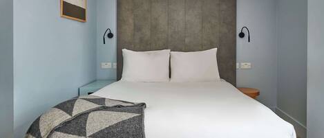 A bedroom with a bed, two bedside tables, a wall-mounted lamp, and a blanket.