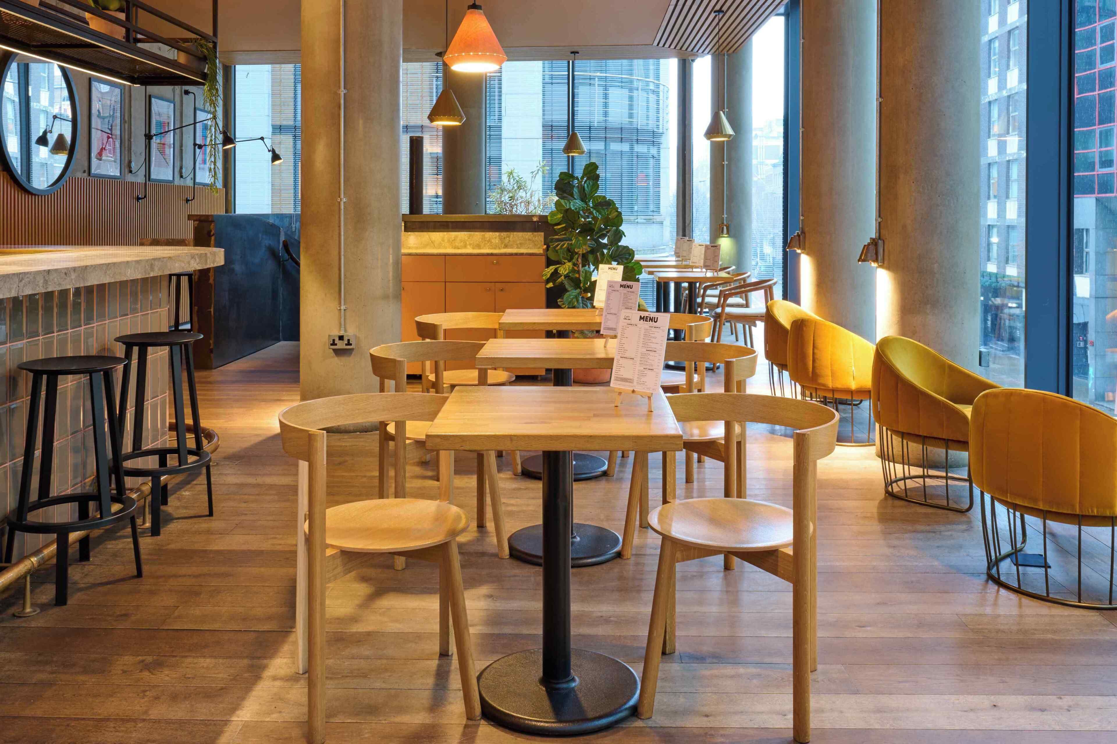 A modern restaurant interior with wooden tables and chairs, a bar area, and large windows offering city views.