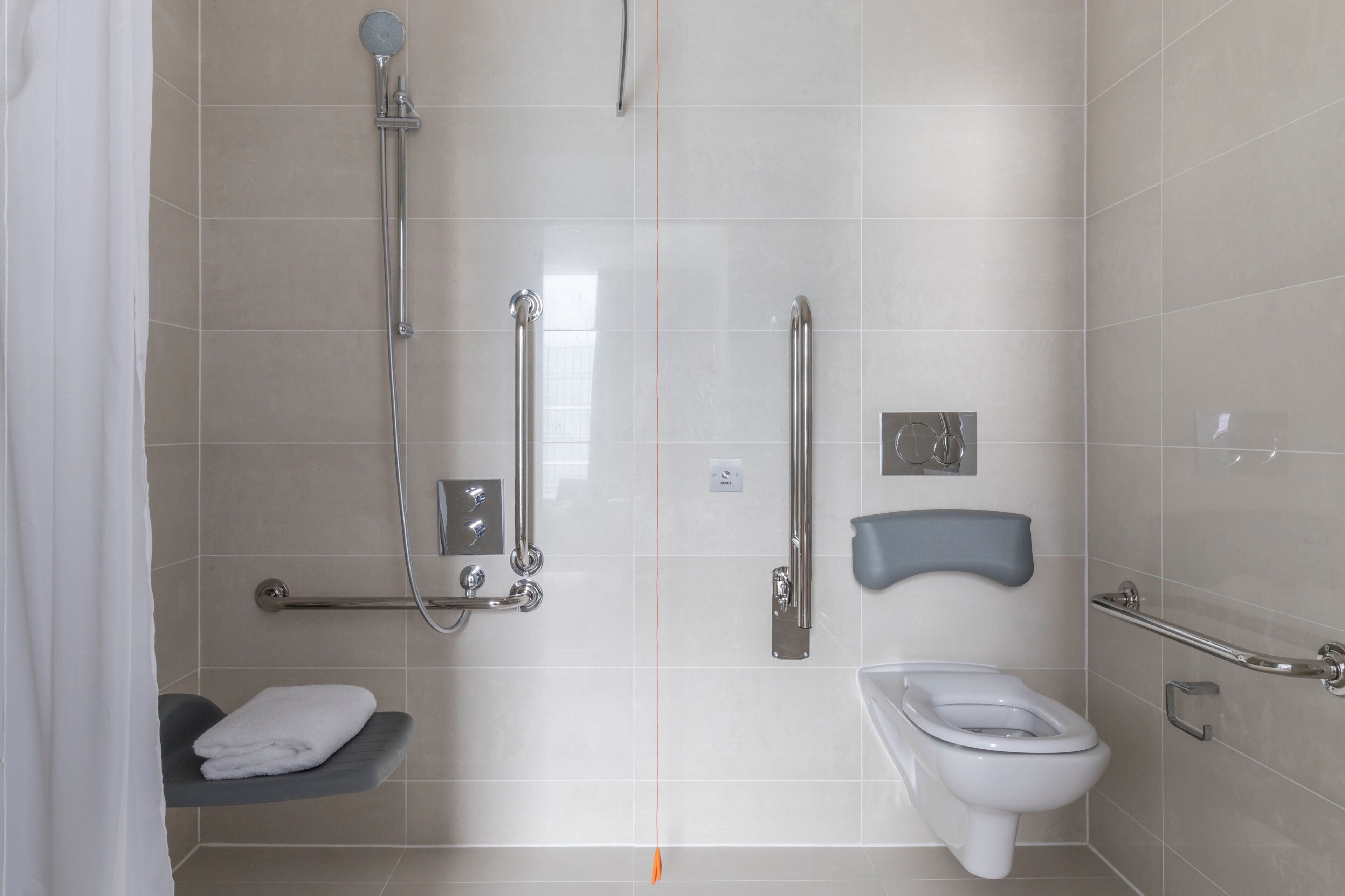 A bathroom with a shower, toilet, grab bars, and a towel rack.