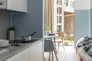 A modern kitchen with a dining area, a view of a building, and a balcony with a chair and plant.