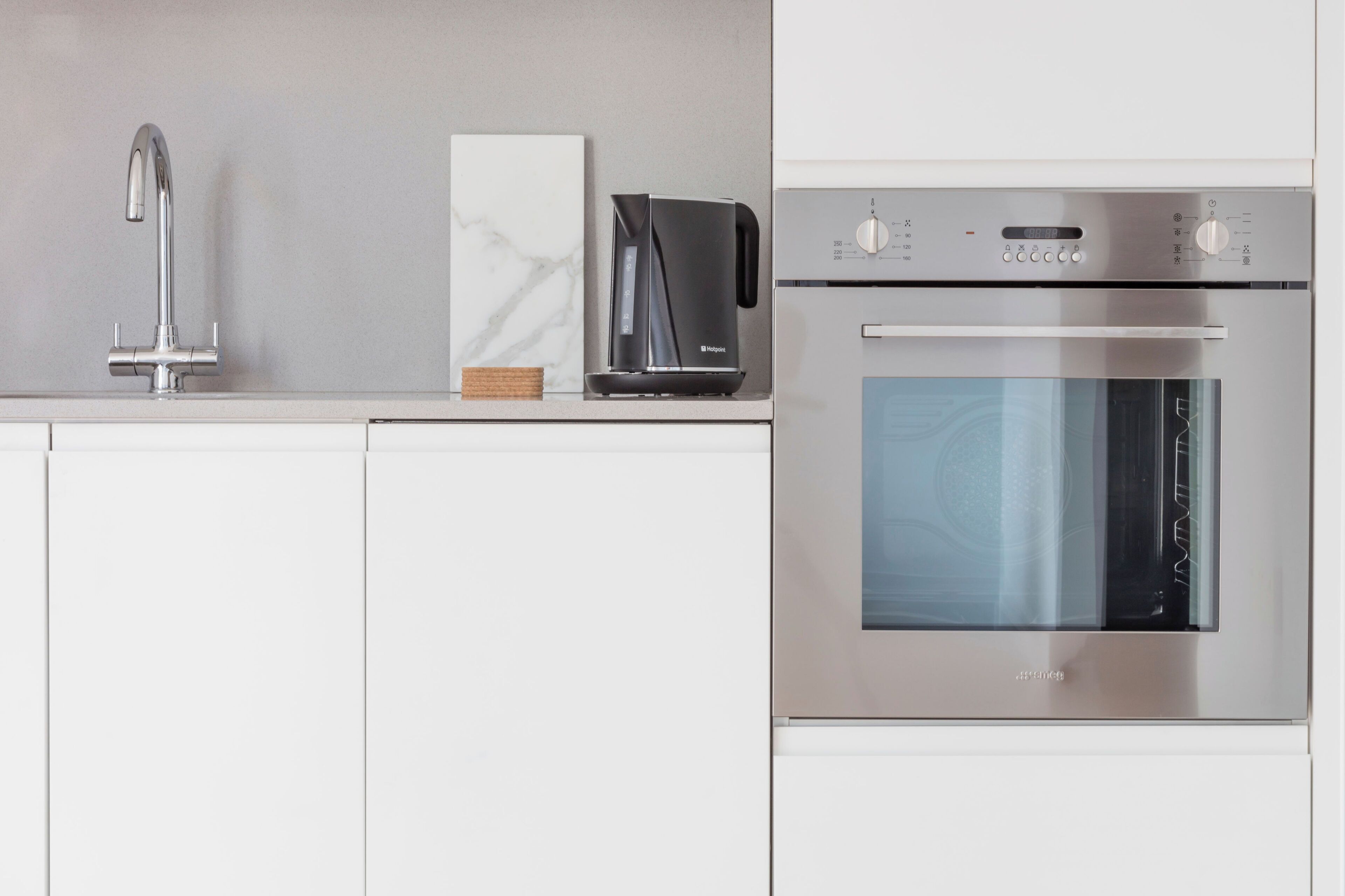 A modern kitchen with a stainless steel range hood, a built-in oven, and a single-basin sink.