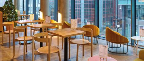 A modern cafe with wooden tables and chairs, menu stands, and large windows offering a view of the cityscape.