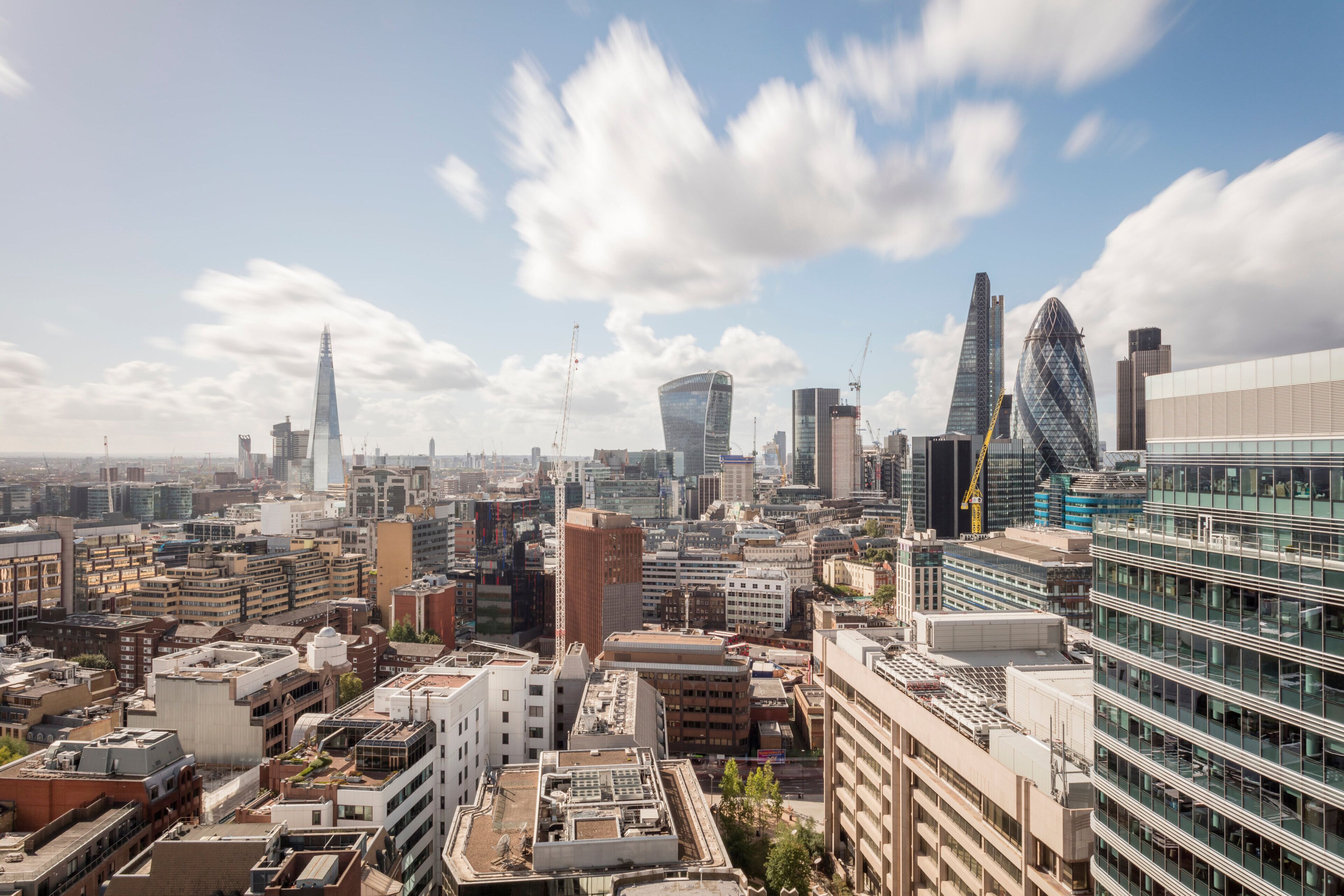 A cityscape with modern buildings, including a distinctive spire and a curved glass structure.