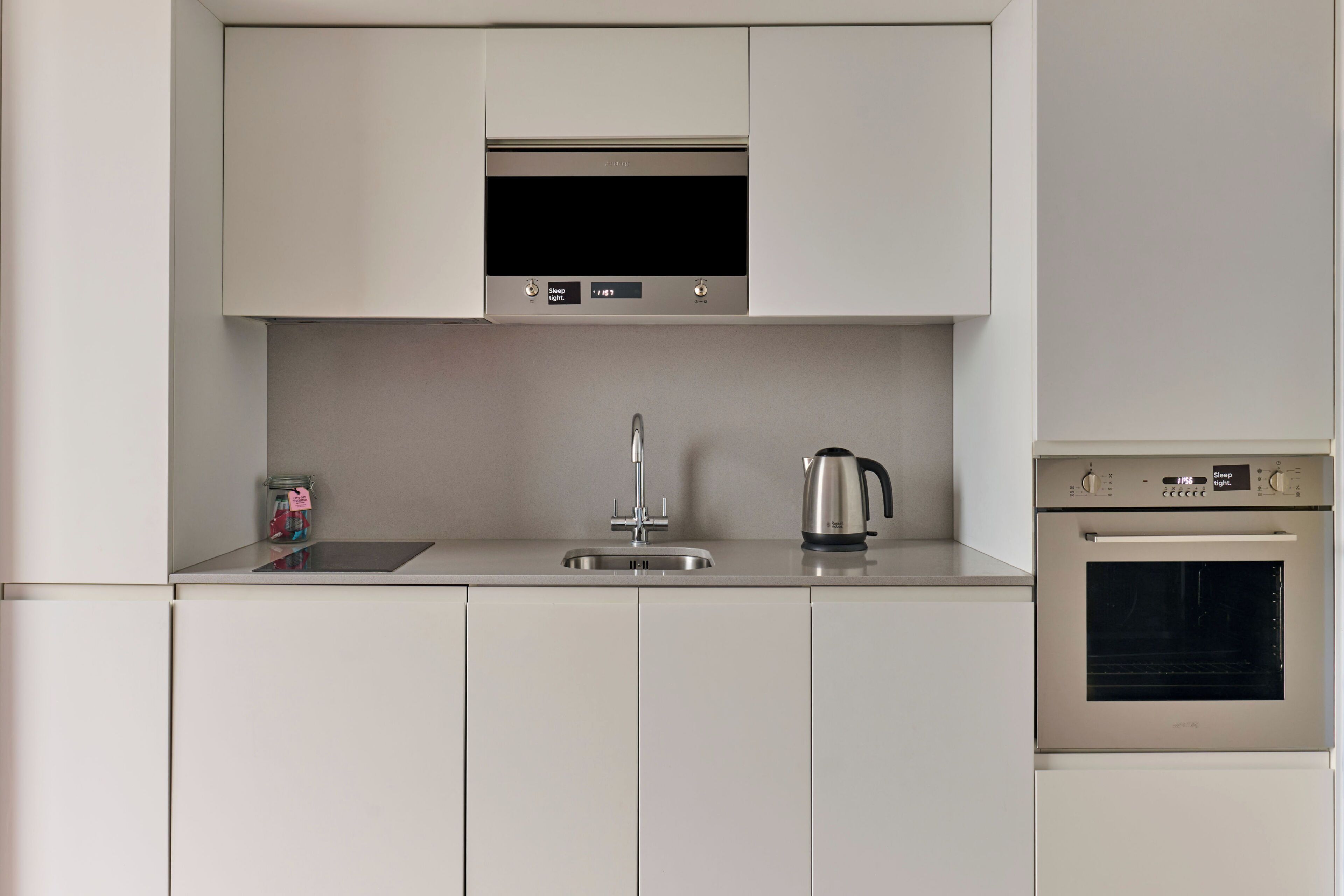 A modern kitchen with a built-in microwave, a kettle, and an oven.