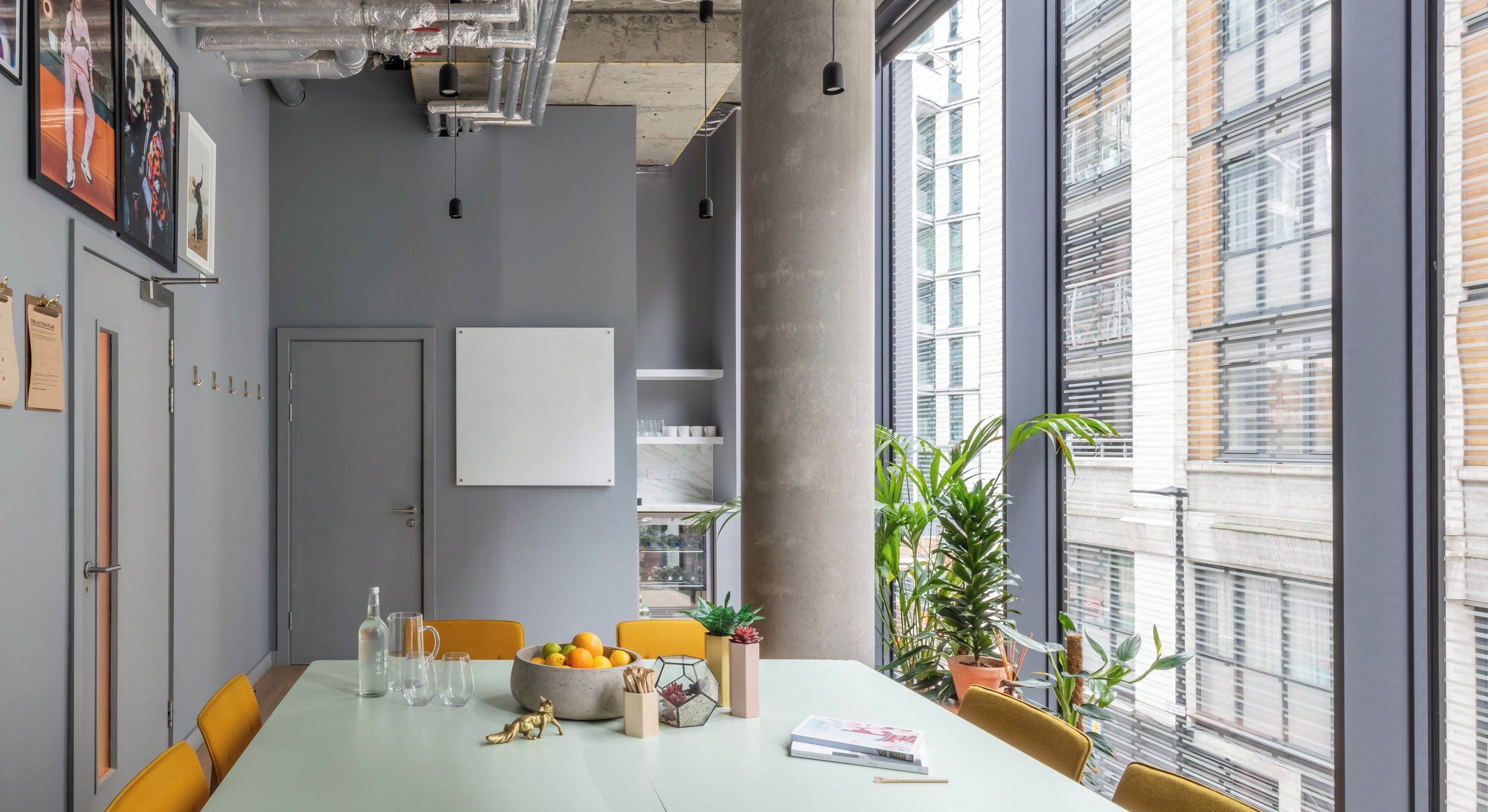 A modern meeting room with a long table, chairs, a whiteboard, and large windows with a city view.
