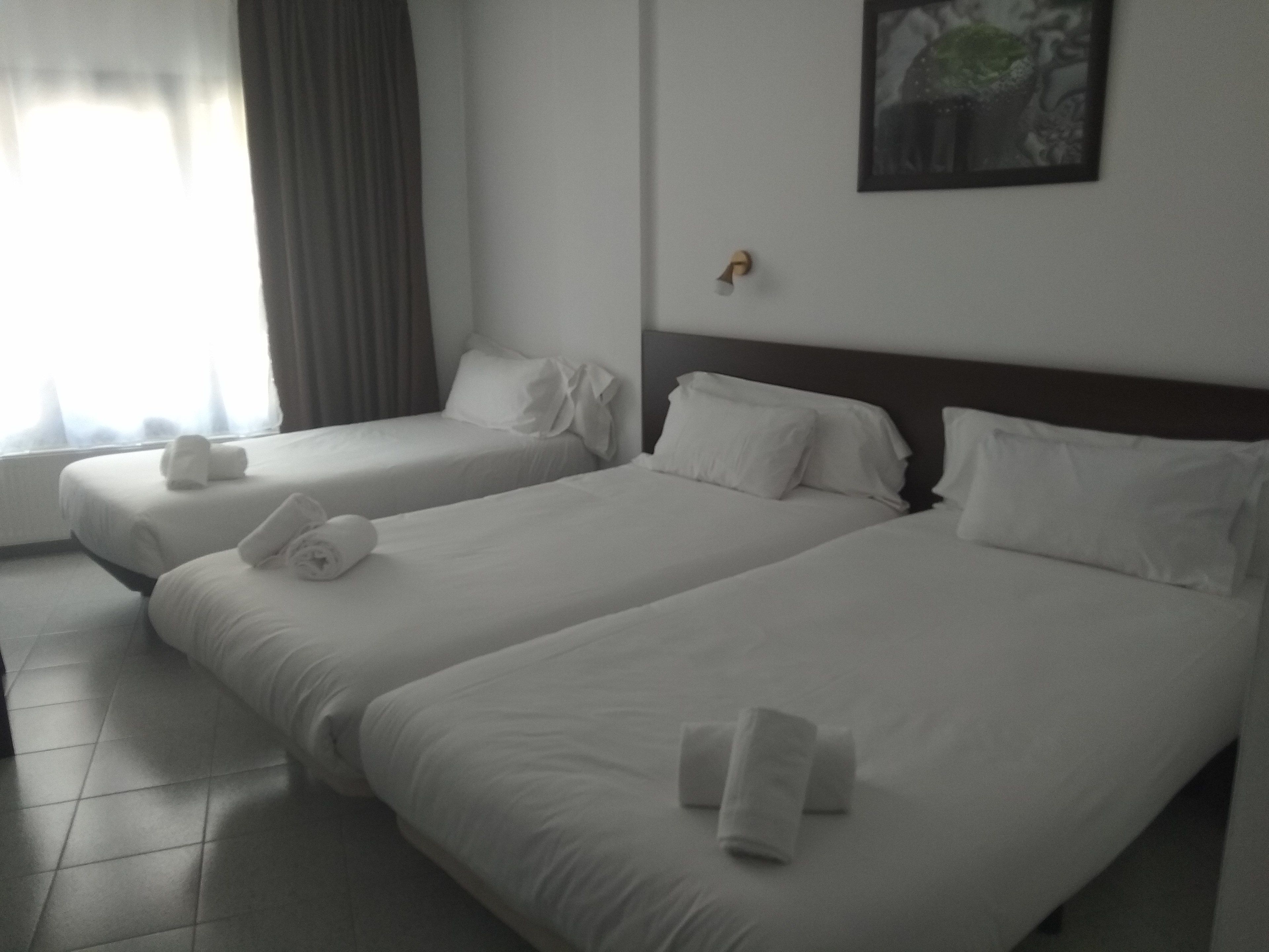 A hotel room with two single beds, each with a pillow and a rolled towel.