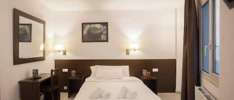 A hotel room with a bed, two bedside tables, a desk, a chair, and two wall-mounted lamps.