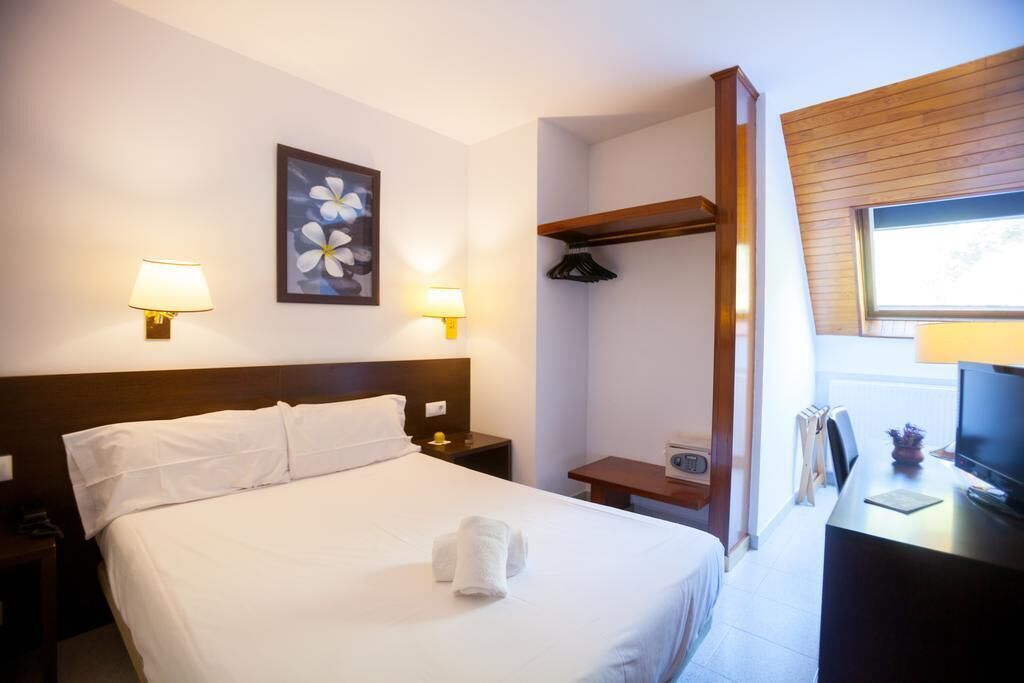 A hotel room with a bed, two bedside lamps, a desk with a computer, a TV, and a window.