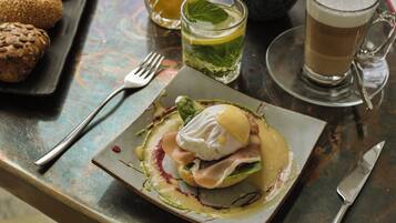 A plated dish with a poached egg, greens, and a sauce, accompanied by a glass of beer and a cup of tea on a table.