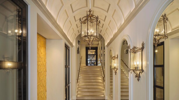 Un vaste hall d’entrée avec un escalier en marbre, des appliques murales décoratives et un banc.