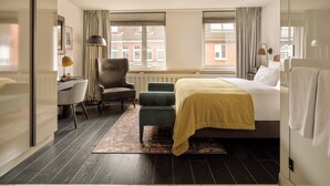 A hotel room with a bed, a desk, a chair, and a view of the city through large windows. - The Nikolai Hotel Hamburg, Leonardo Limited Edition (Hamburg)