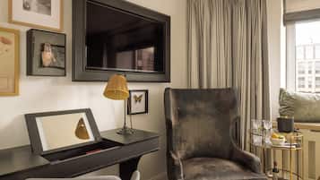 Una sala de estar moderna con un televisor de pantalla plana grande montado en la pared, un escritorio de madera oscura con una lámpara, un sillón cómodo y una mesa de centro de vidrio con objetos decorativos.