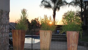 Three large, rust-colored planters with greenery, positioned on a concrete surface near a metal fence, with a body of water and trees in the background. - Country Park (Muldersdrift)