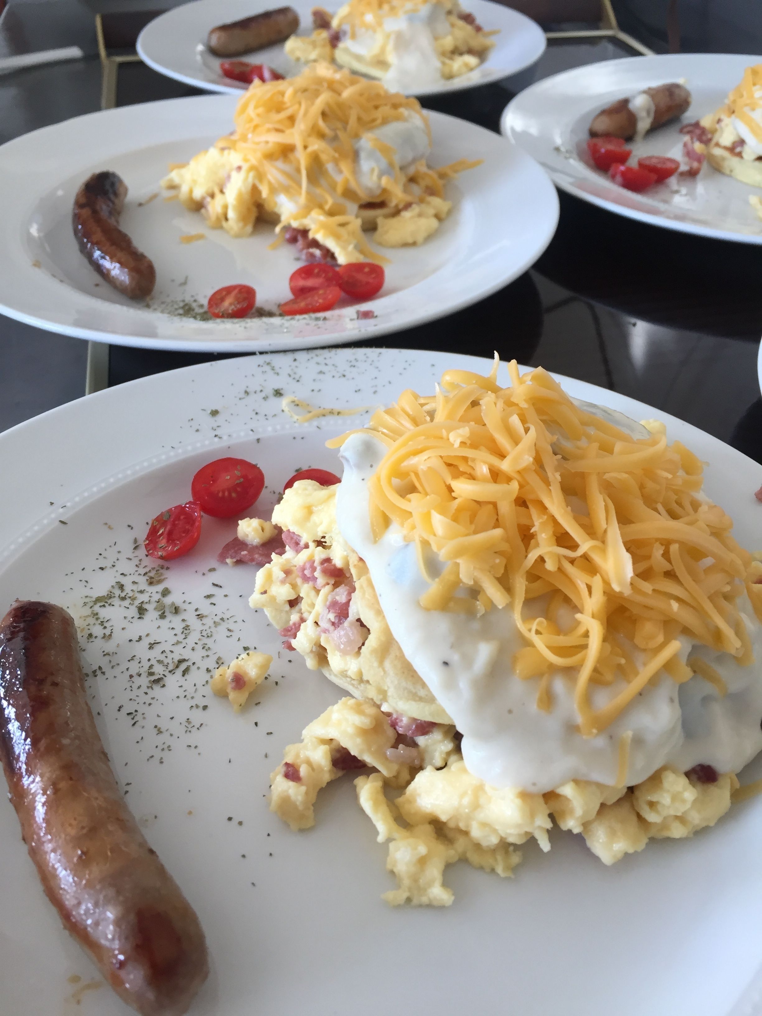 A table with plates of food, including sausages, scrambled eggs, and cheese.