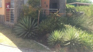 A building with a stone facade, a covered porch, and a small garden with various plants. - Country Park (Muldersdrift)