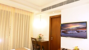A hotel room with a bed, a desk with a chair, a television mounted on the wall, and a window with curtains. - Visitel - A Boutique Hotel (Kolkata)