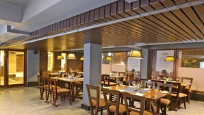 A restaurant with wooden tables and chairs, a wooden ceiling, and hanging lamps. - Visitel - A Boutique Hotel (Kolkata)