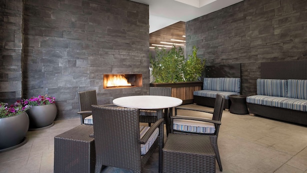 Un espace extérieur aménagé en terrasse, avec une table ronde et des chaises en osier, un foyer intégré et un coin salon avec des coussins.