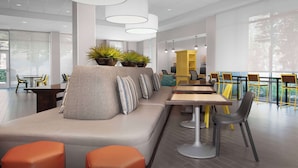 Il s’agit d’un espace intérieur moderne, doté d’un long banc, de tables et de chaises. Des plantes en pot sont disposées sur le banc, et la pièce est baignée de lumière grâce à de grandes fenêtres.