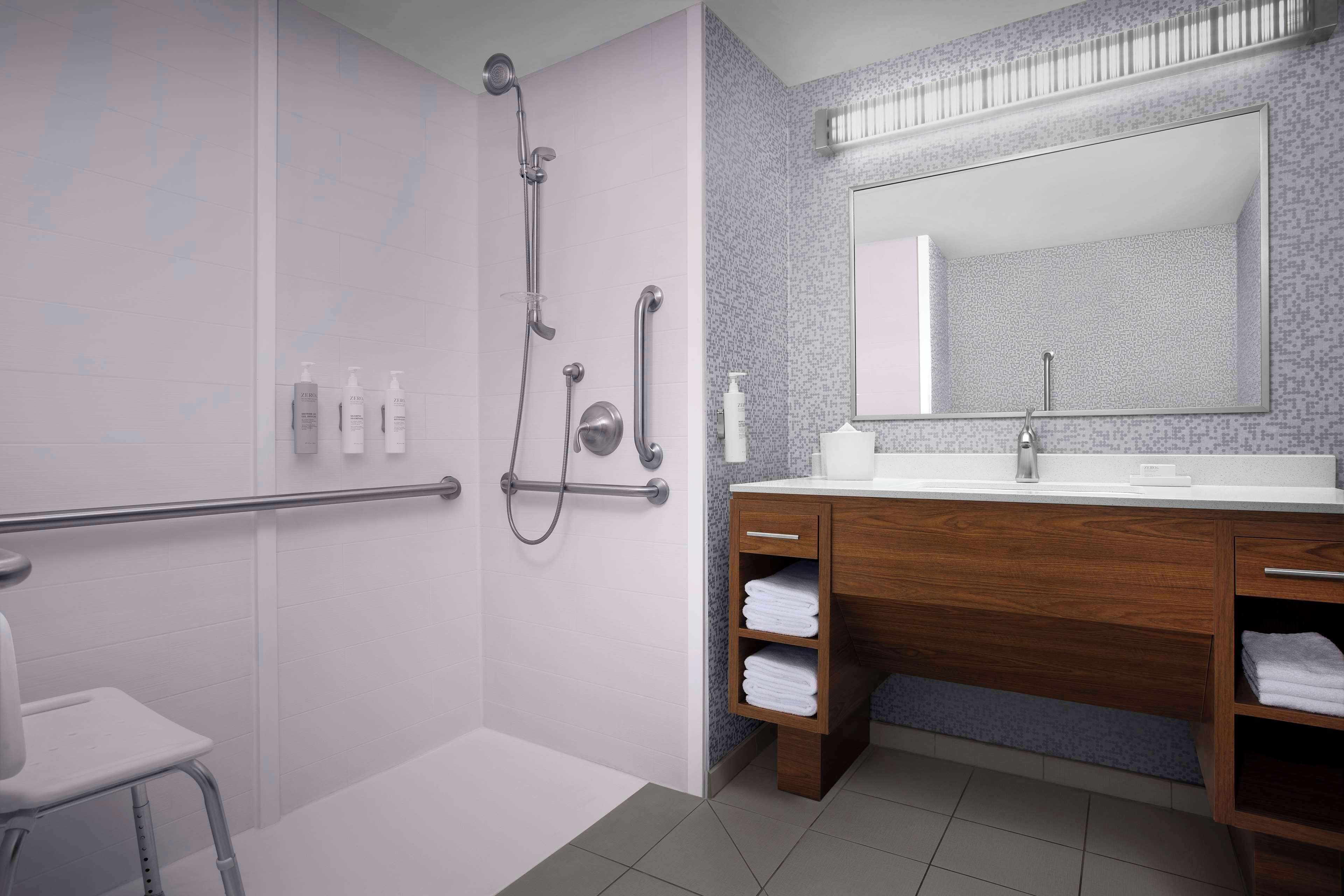 Ein modernes Badezimmer mit einer bodenebenen Dusche, einem Waschtisch mit großem Spiegel und einer Toilette.