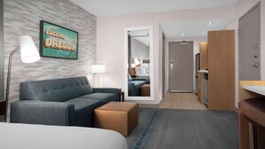 Une chambre d’hôtel comprenant un lit, un canapé, une petite table, une lampe, un miroir et un coin cuisine.