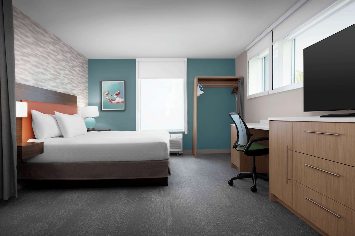 Une chambre d’hôtel avec un lit, un bureau, une télévision et un tableau au mur.