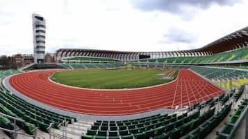 A stadium with a running track, green seating, and a tall building to the left.