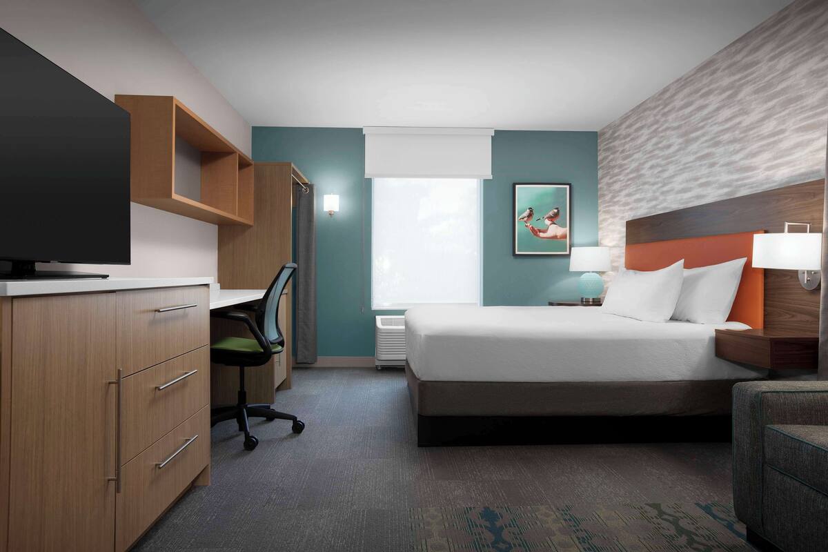 Une chambre d’hôtel avec un lit, un bureau, une chaise, une télévision et un tableau au mur.