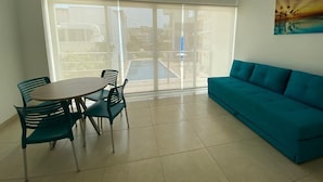 Une pièce avec un balcon, une table ronde entourée de chaises et un canapé de couleur turquoise.
