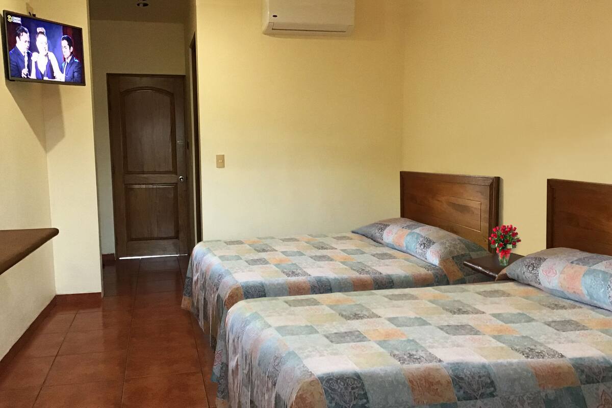 Une chambre d’hôtel avec deux lits, un téléviseur fixé au mur et une porte donnant sur une autre pièce.