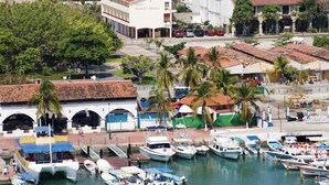 Un port de plaisance où sont amarrés plusieurs bateaux, un hôtel appelé « Hotel Huatuco México » en arrière-plan, et une ville côtière avec des palmiers et une architecture traditionnelle.