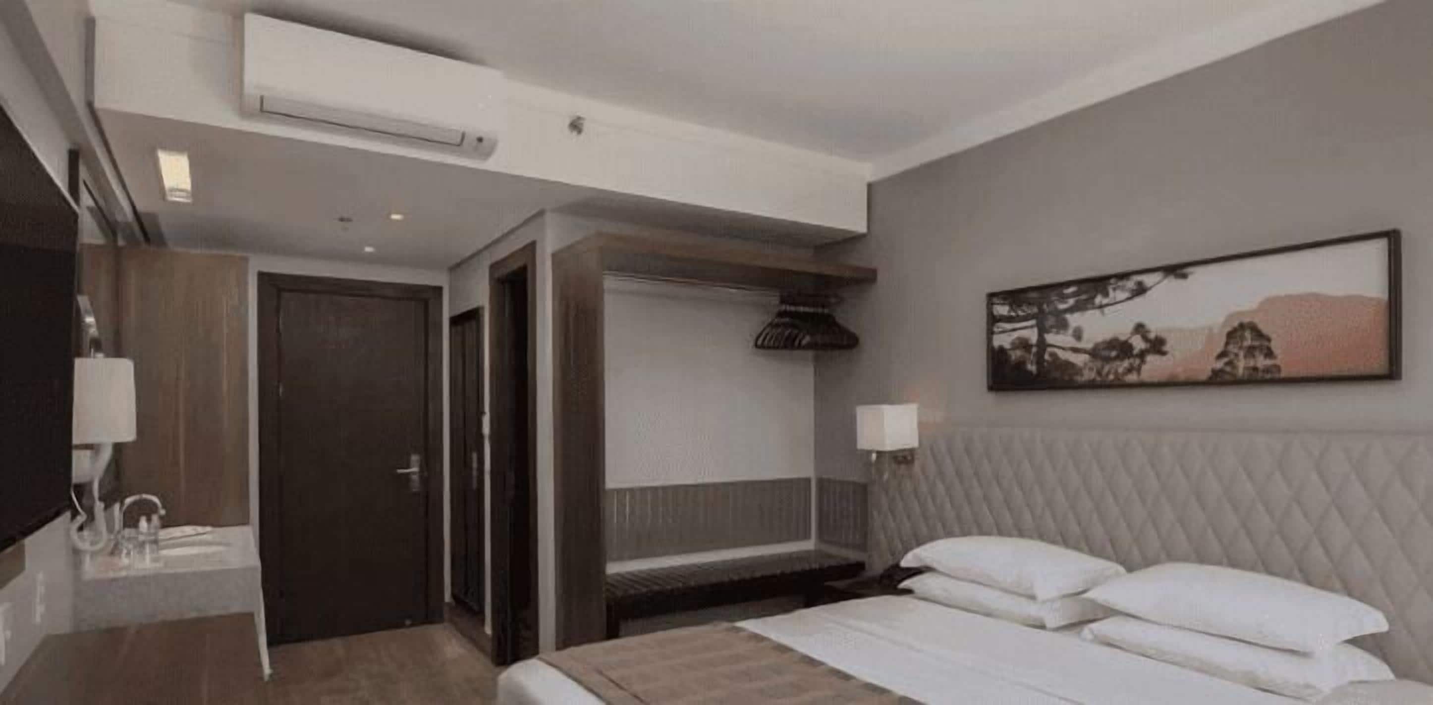 Een hotelkamer met een bed, nachtkastje, lamp en een schilderij aan de muur.