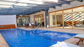 A swimming pool with a glass enclosure, wooden deck, and lounge chairs. - Prodigy Gramado by Wish (Gramado)