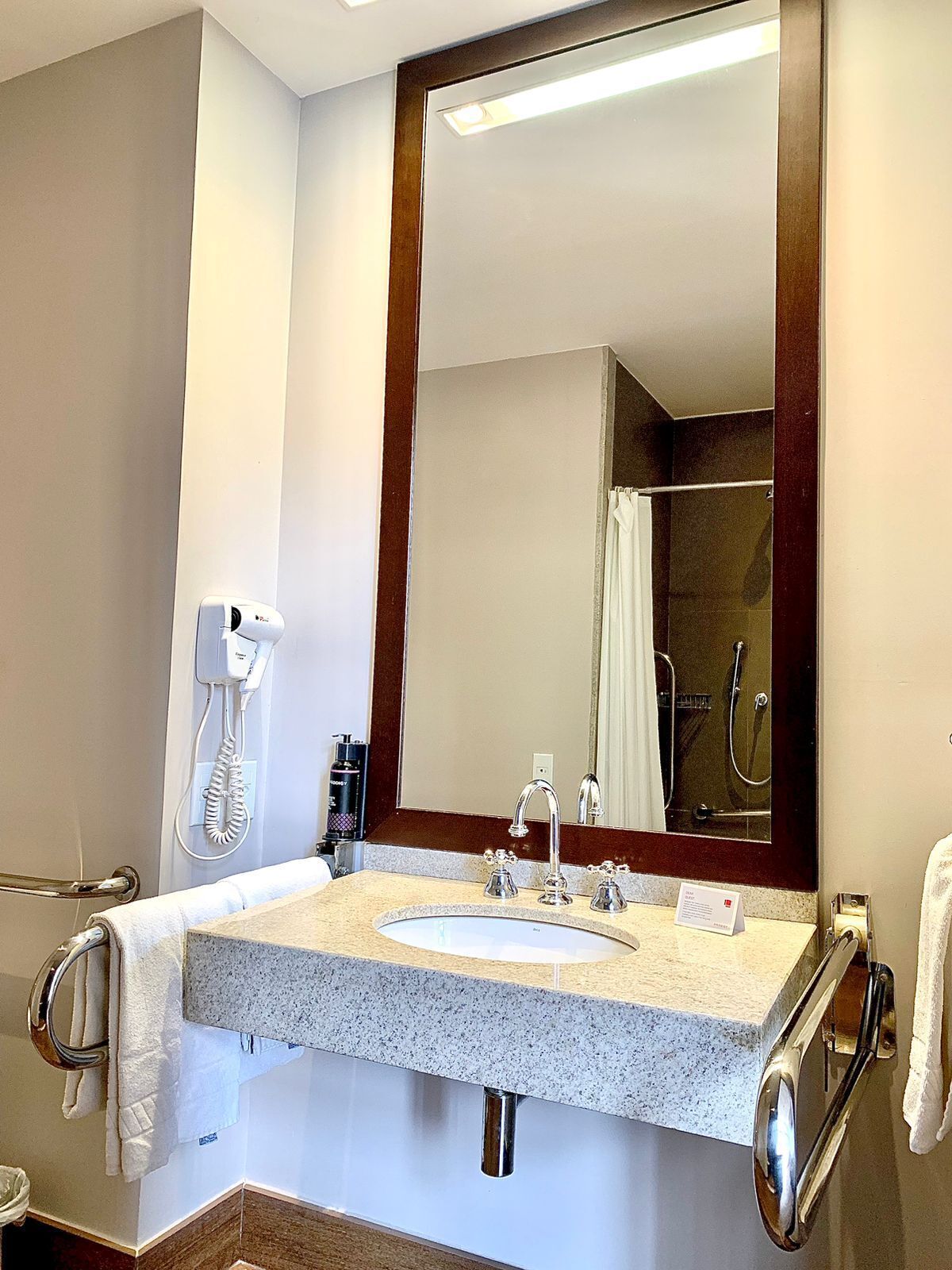 A bathroom with a sink, mirror, towel rack, and a shower visible in the reflection.