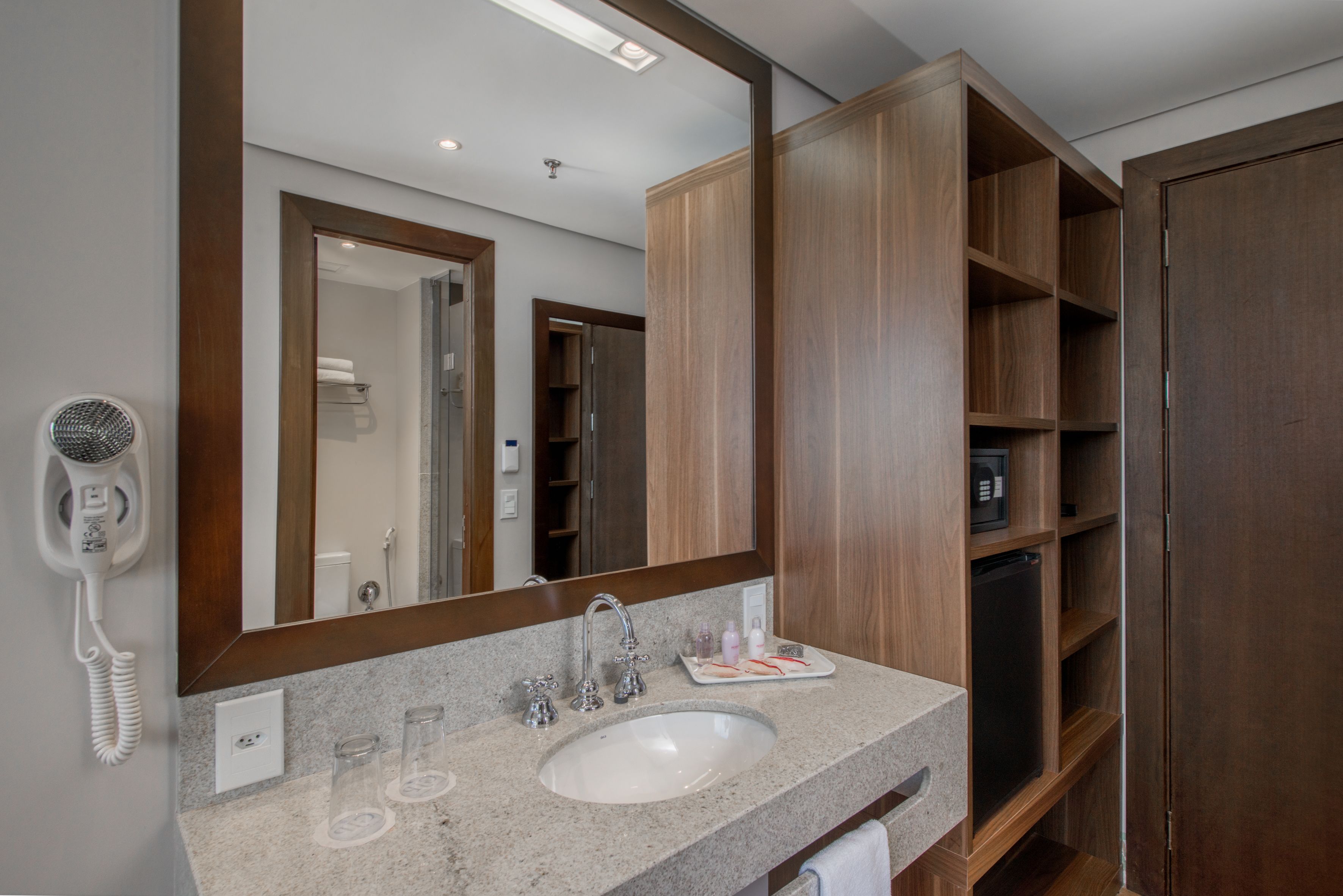 Un baño con un espejo grande, un lavamanos, un secador de pelo y estantes de madera.