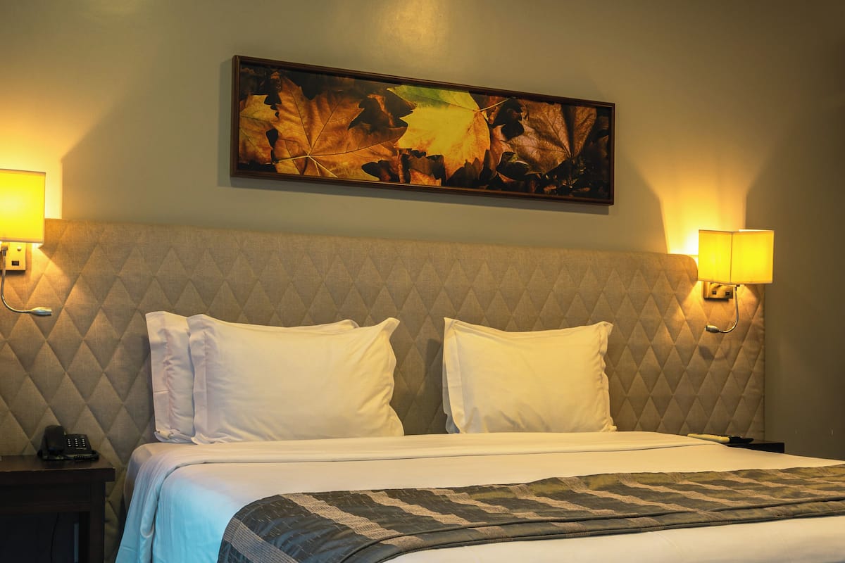 Una habitación de hotel con una cama grande, dos lámparas de noche, una mesita de noche con un teléfono y un cuadro en la pared.