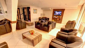 Un hall d’hôtel moderne avec des canapés en cuir, une table basse en bois et un téléviseur à écran plat fixé au mur.