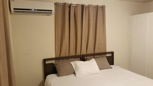 Une chambre d’hôtel avec un lit, une tête de lit, une fenêtre avec des rideaux et un appareil de climatisation.