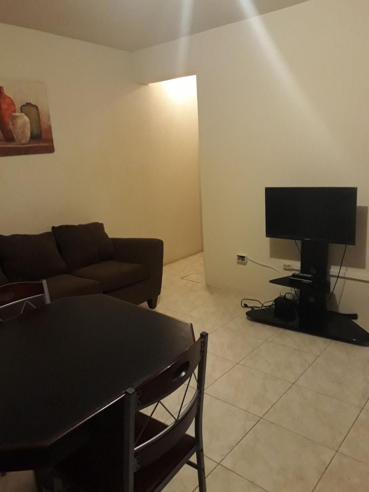 A living room with a dark wooden table and chairs, a brown sofa, and a flat-screen TV on a stand.
