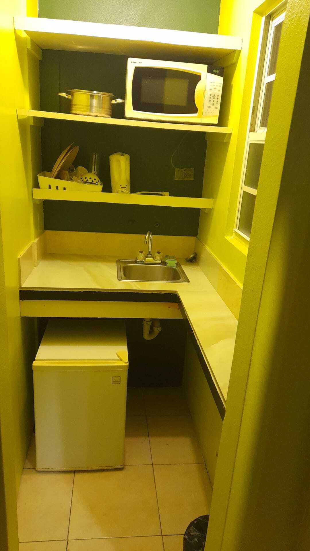 Cocina compacta con microondas, lavamanos y nevera pequeña.