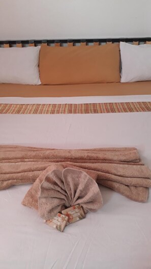 A bed with a striped headboard, a brown pillow, and a white pillow. - Haven House Apartments (Oistins)
